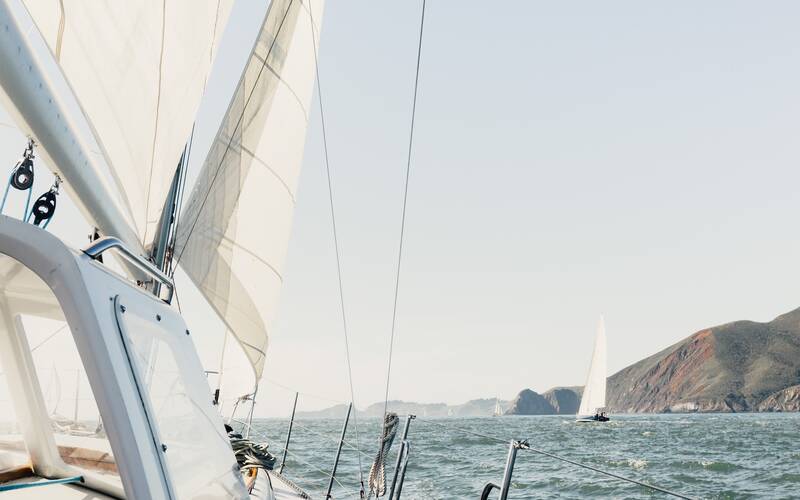 Zeilboot op het water met een andere zeilboot en heuvelachtige kust op de achtergrond
