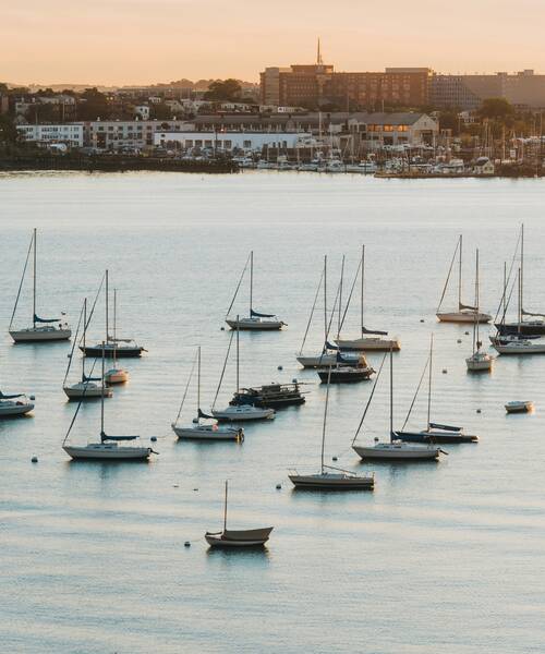 Zeilboten voor anker op rustig water bij een haven tijdens zonsondergang